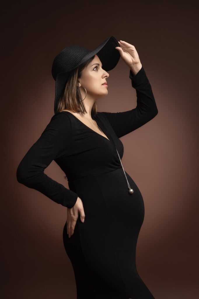 Future maman en robe noire et chapeau sur fond brun
