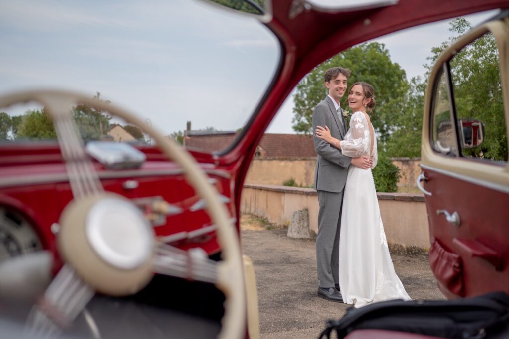 Les mariés vus à travers une voiture ancienne rouge
