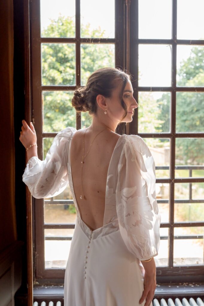 Mariée de dos devant une grande fenêtre, robe dos nu