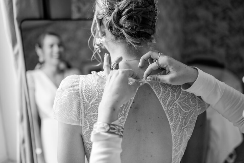 Une proche boutonne le dos de la robe de mariée, noir et blanc